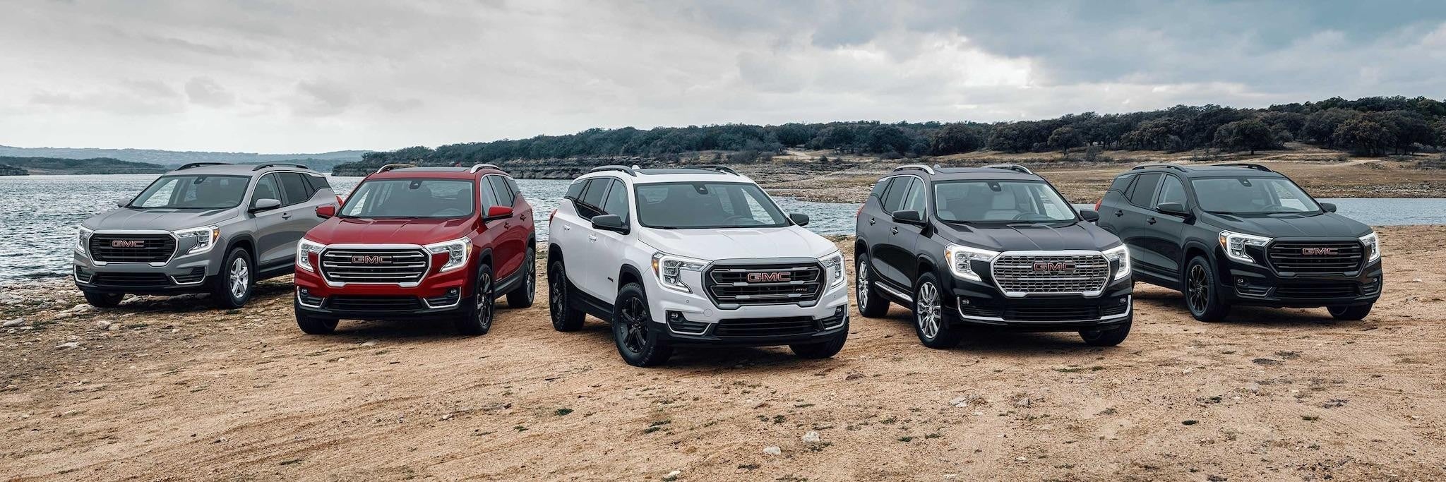 Five GMC Terrain vehicals parked on the dirt next to a lake