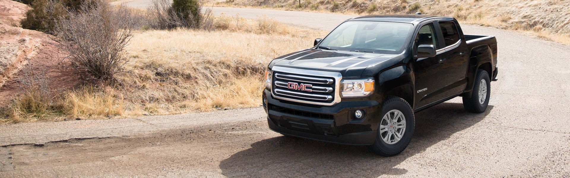 A black GMC Canyon driving on a country road